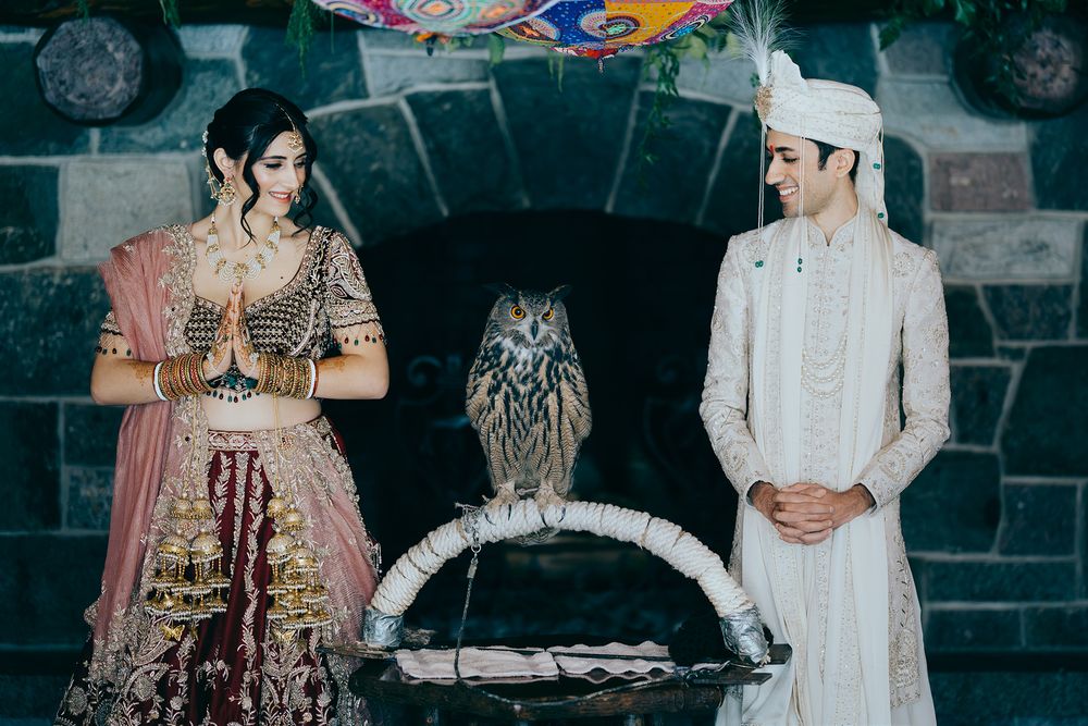 Indian bride and groom in traditional attire posing with an owl at their wedding ceremony.