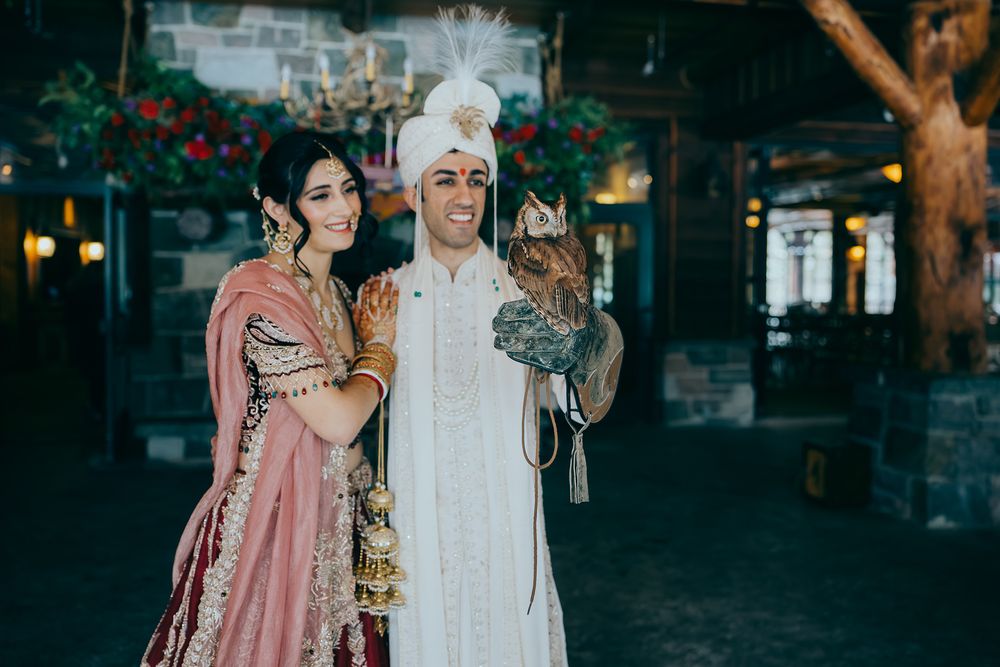 Couple in traditional South Asian wedding attire posing with an owl outdoors.