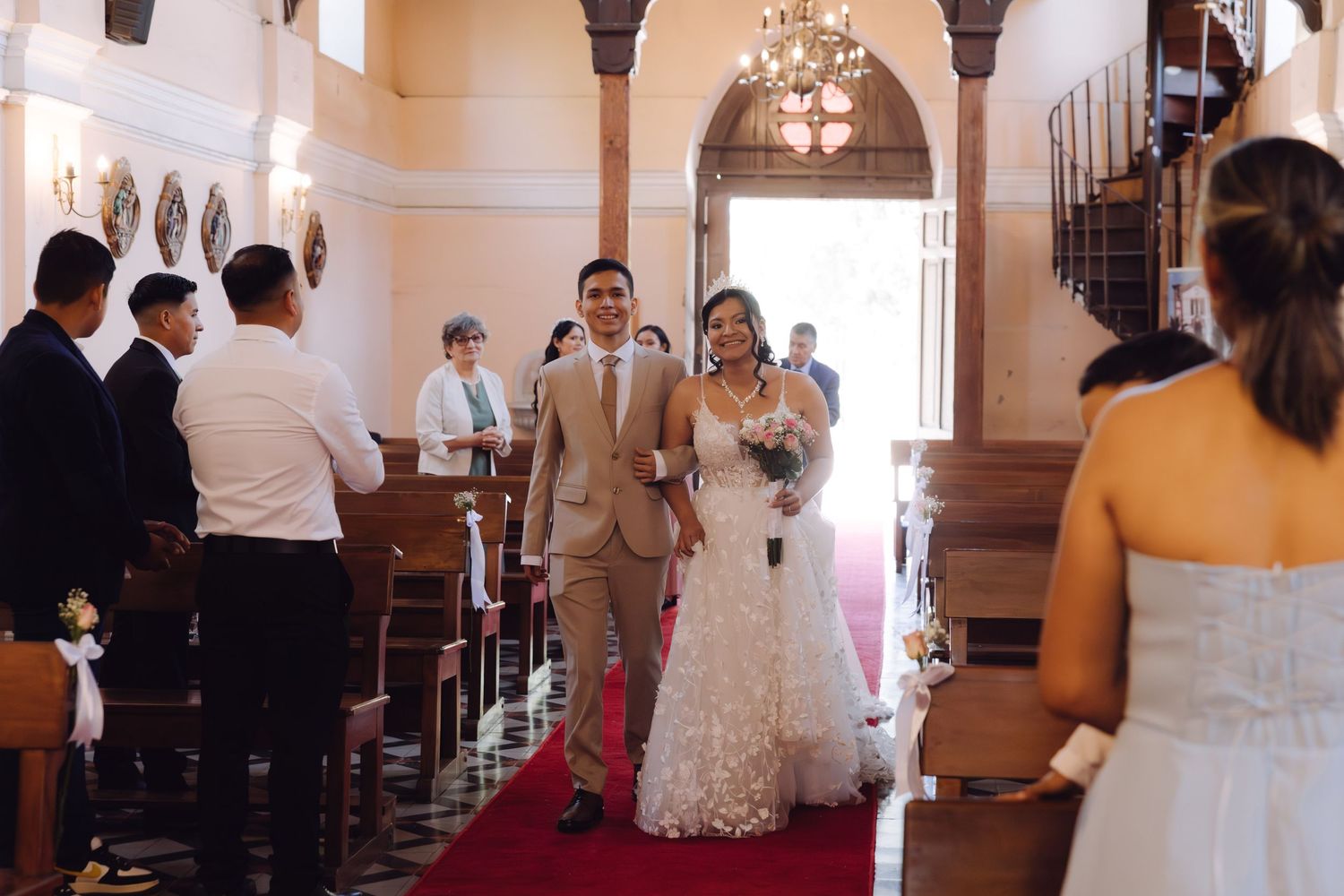 Newlyweds walking back down church aisle after wedding ceremony on red carpet.