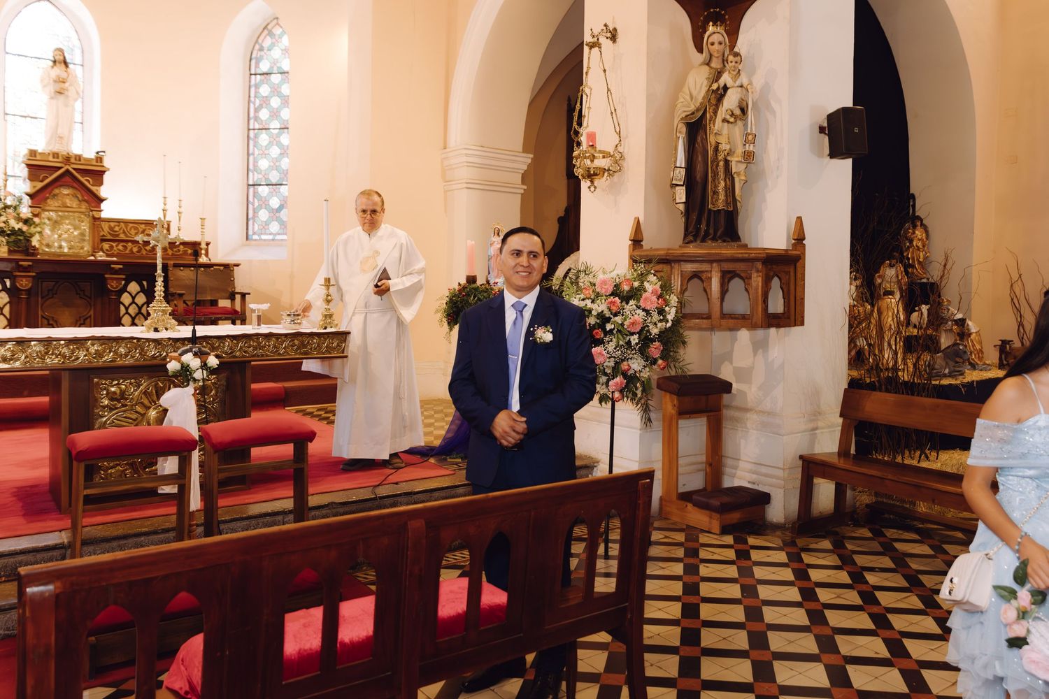 Groom in blue suit standing at ornate church altar awaiting bride during ceremony.