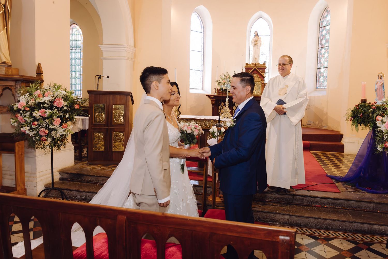 Bride and groom exchange vows at the altar during a church wedding ceremony with a priest officiating.