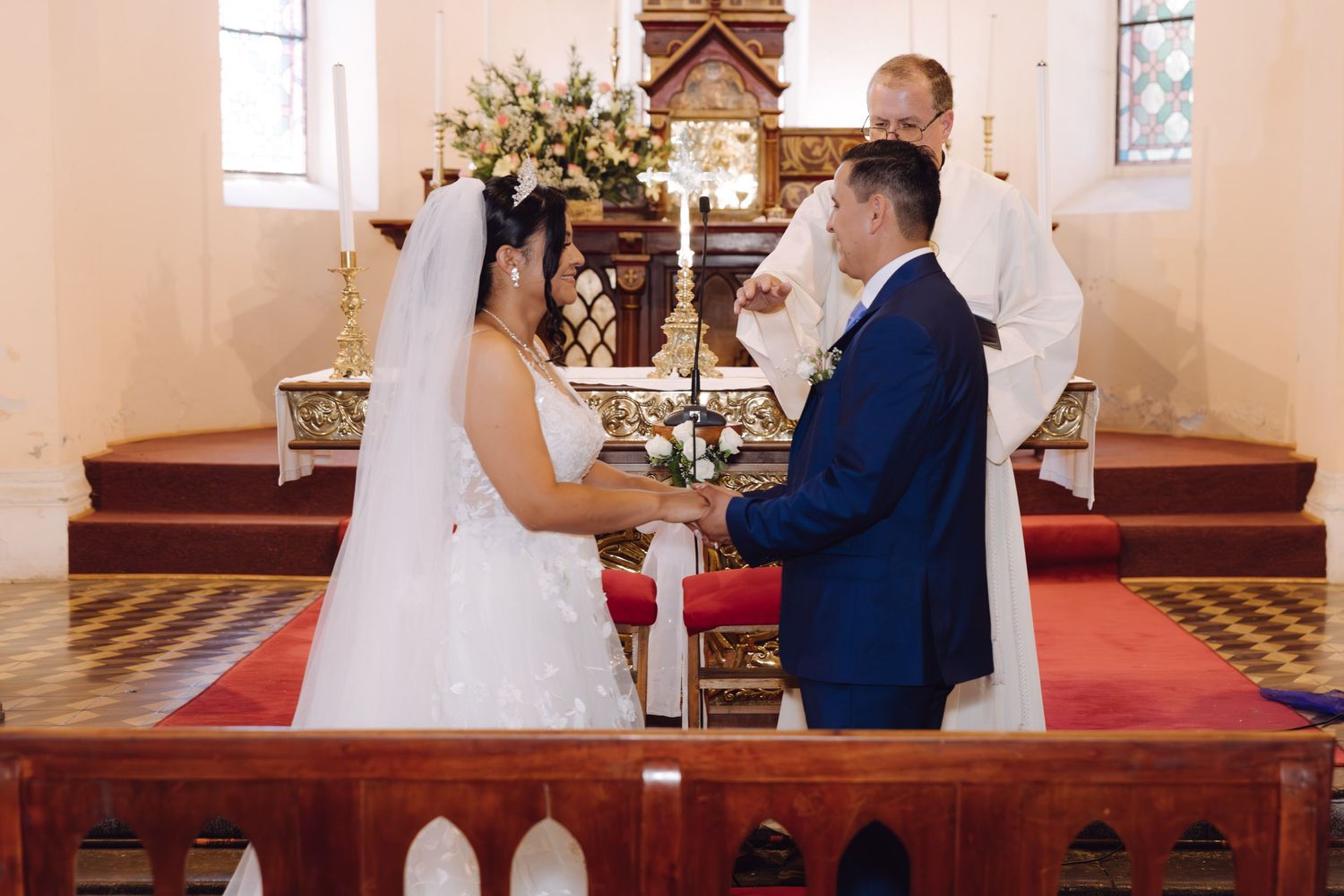 Bride and groom exchange rings at the altar as priest performs the wedding ceremony in a church.