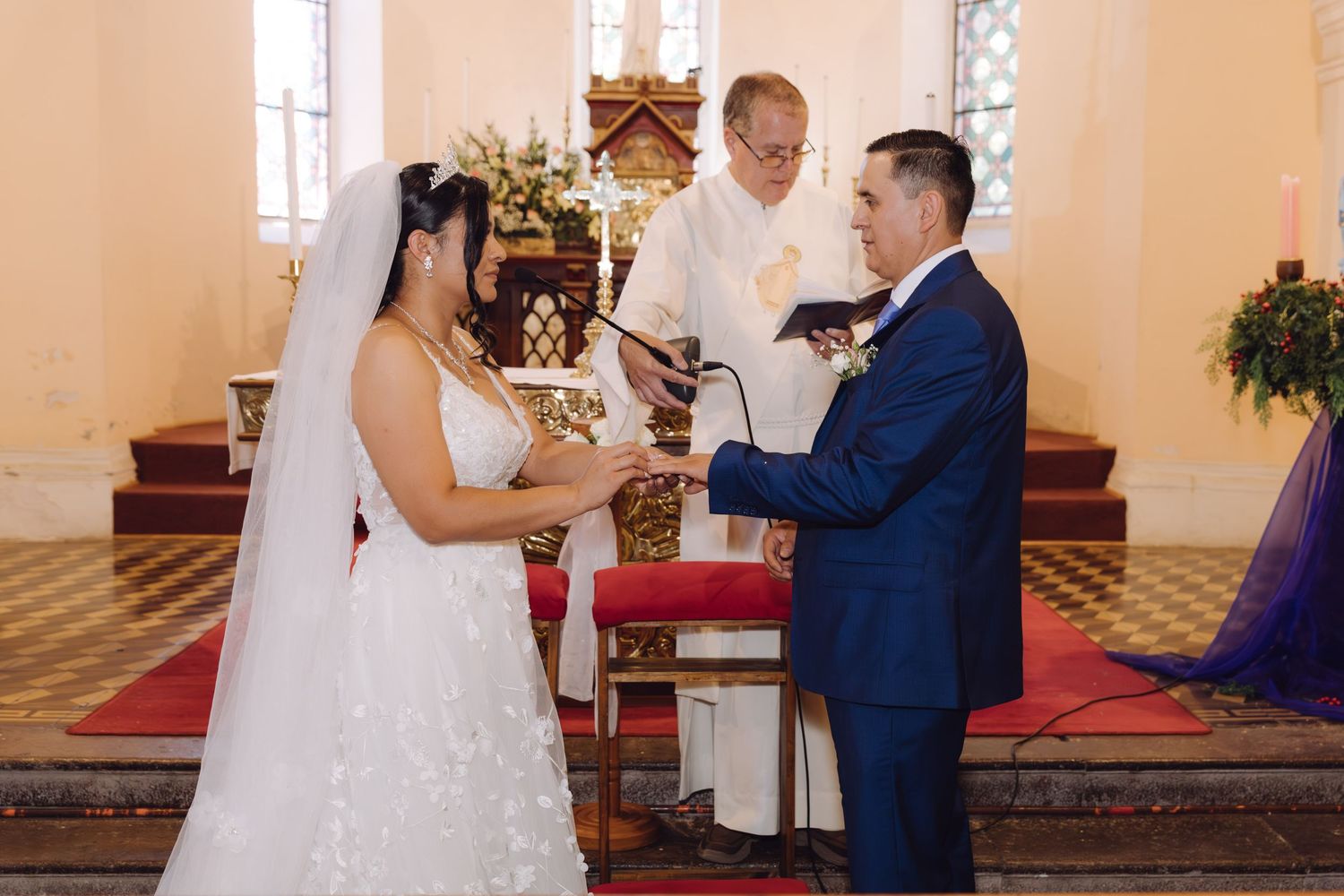 Bride and groom hold hands as officiant reads vows during elegant church wedding ceremony.