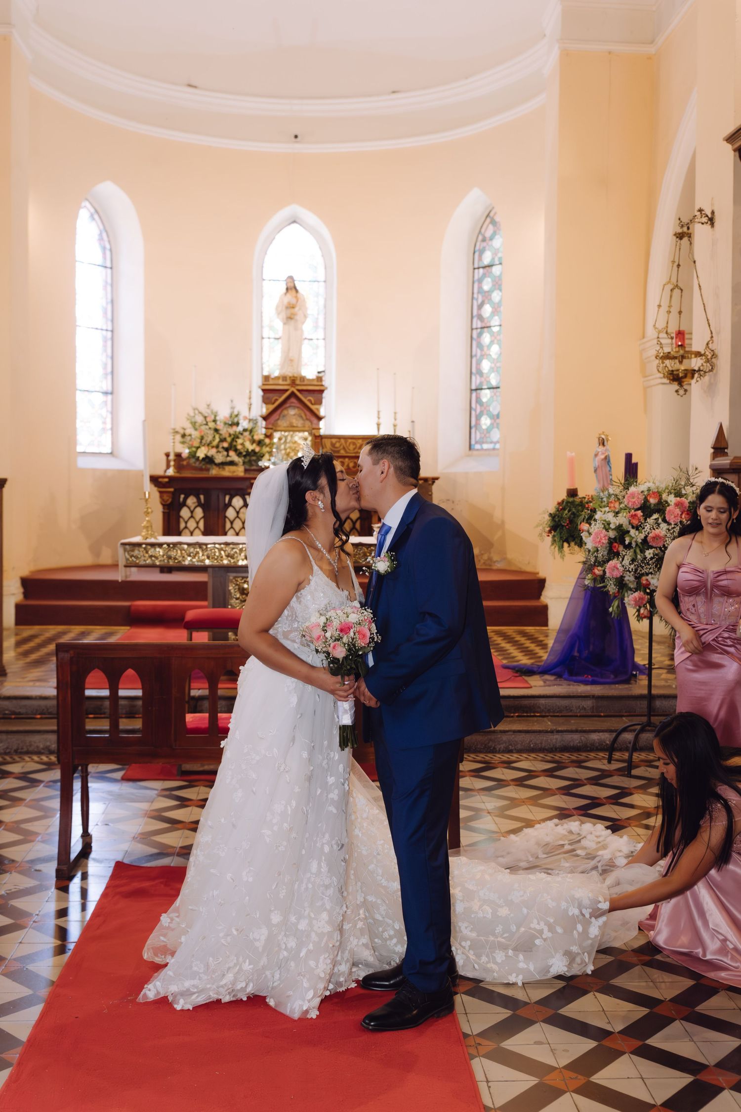 Newlyweds share first kiss on red carpet aisle in beautiful Catholic church ceremony.