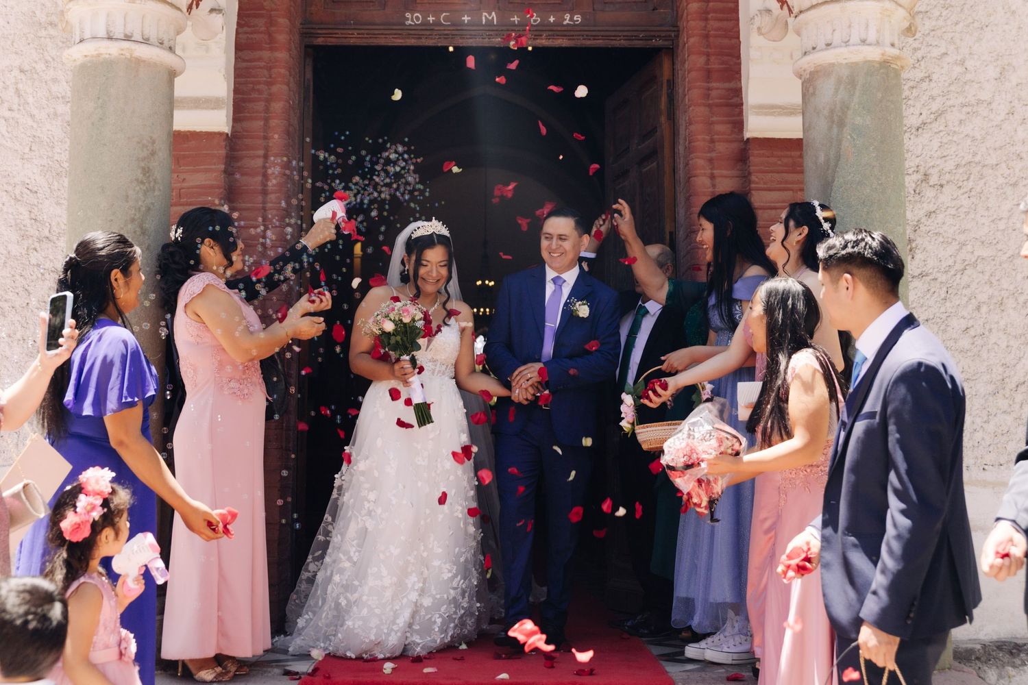 Newlyweds exit church as guests shower them with colorful rose petal confetti celebration.
