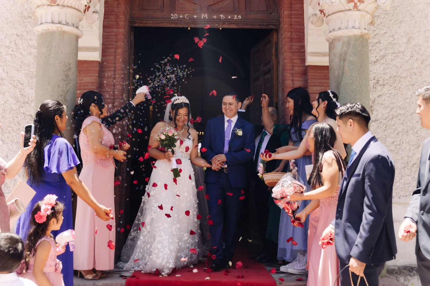 Bride and groom exit church as guests toss rose petals in joyful wedding celebration.