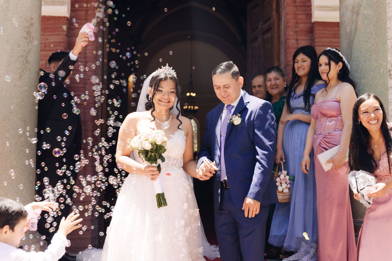 Smiling bride and groom walk through magical bubble send-off outside church after ceremony.