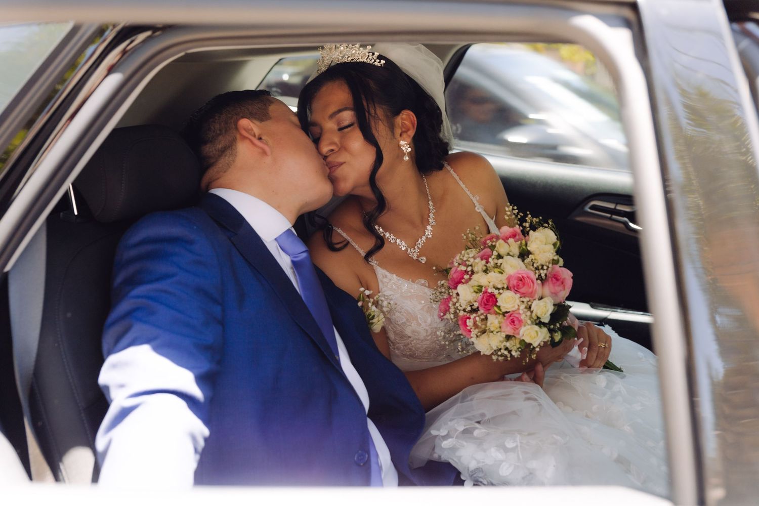 Groom kisses bride tenderly in wedding car as she holds a colorful bridal bouquet.