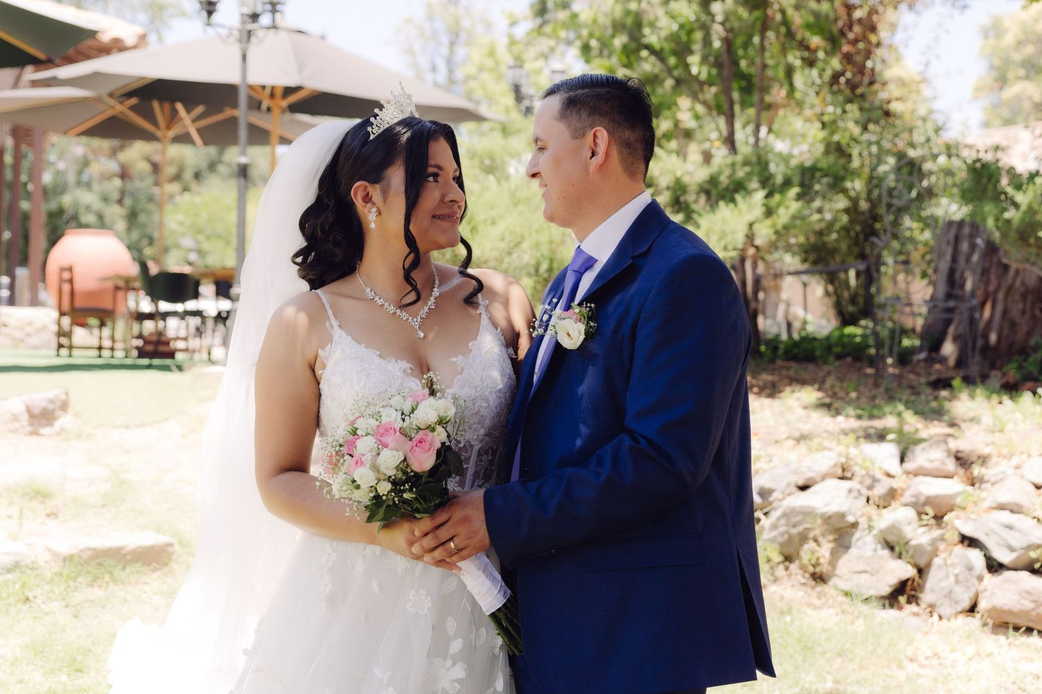 Bride in white gown and groom in blue suit share a tender outdoor moment.