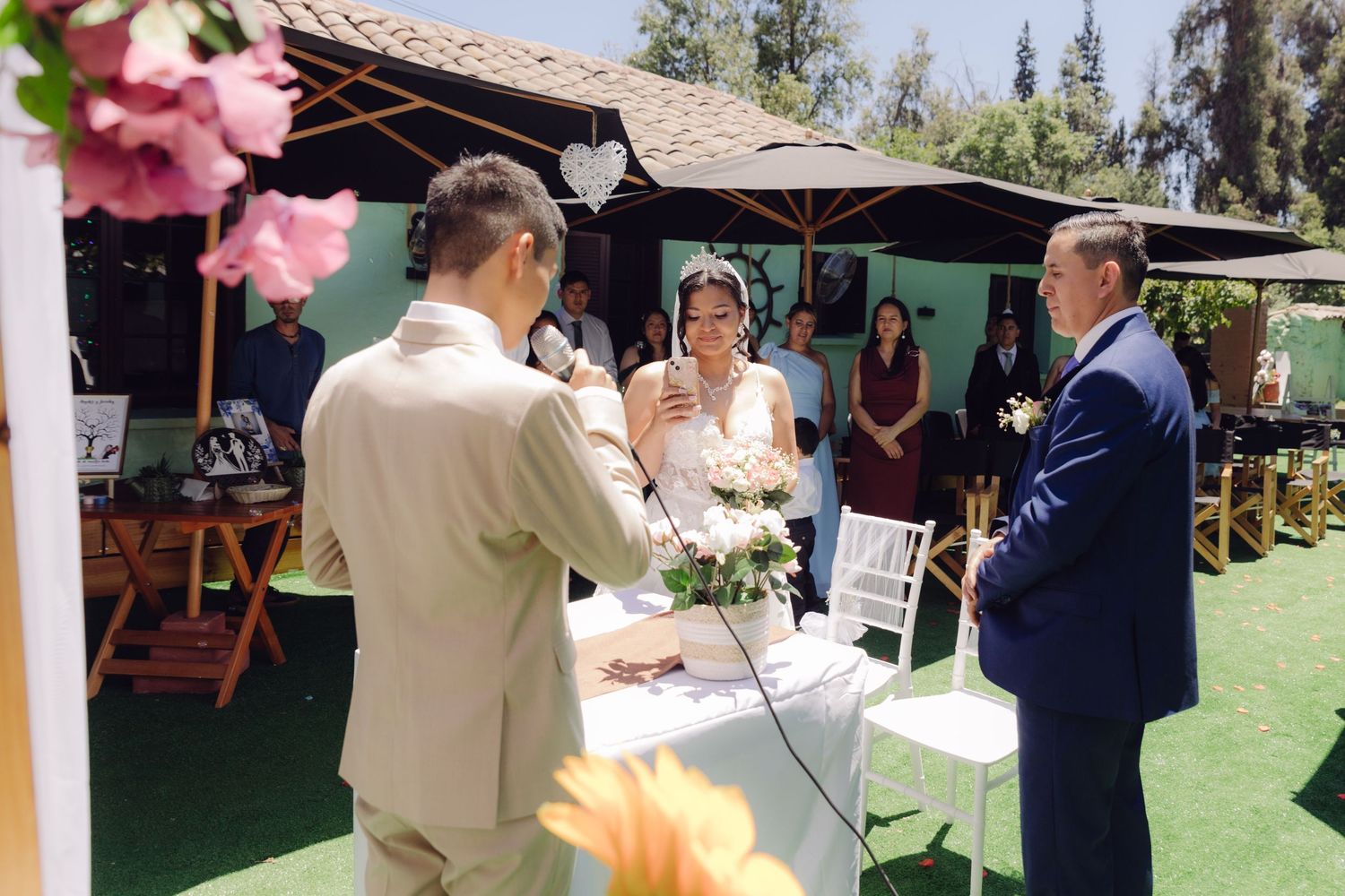 Officiant speaks at outdoor wedding ceremony as bride and groom stand at decorated altar table.