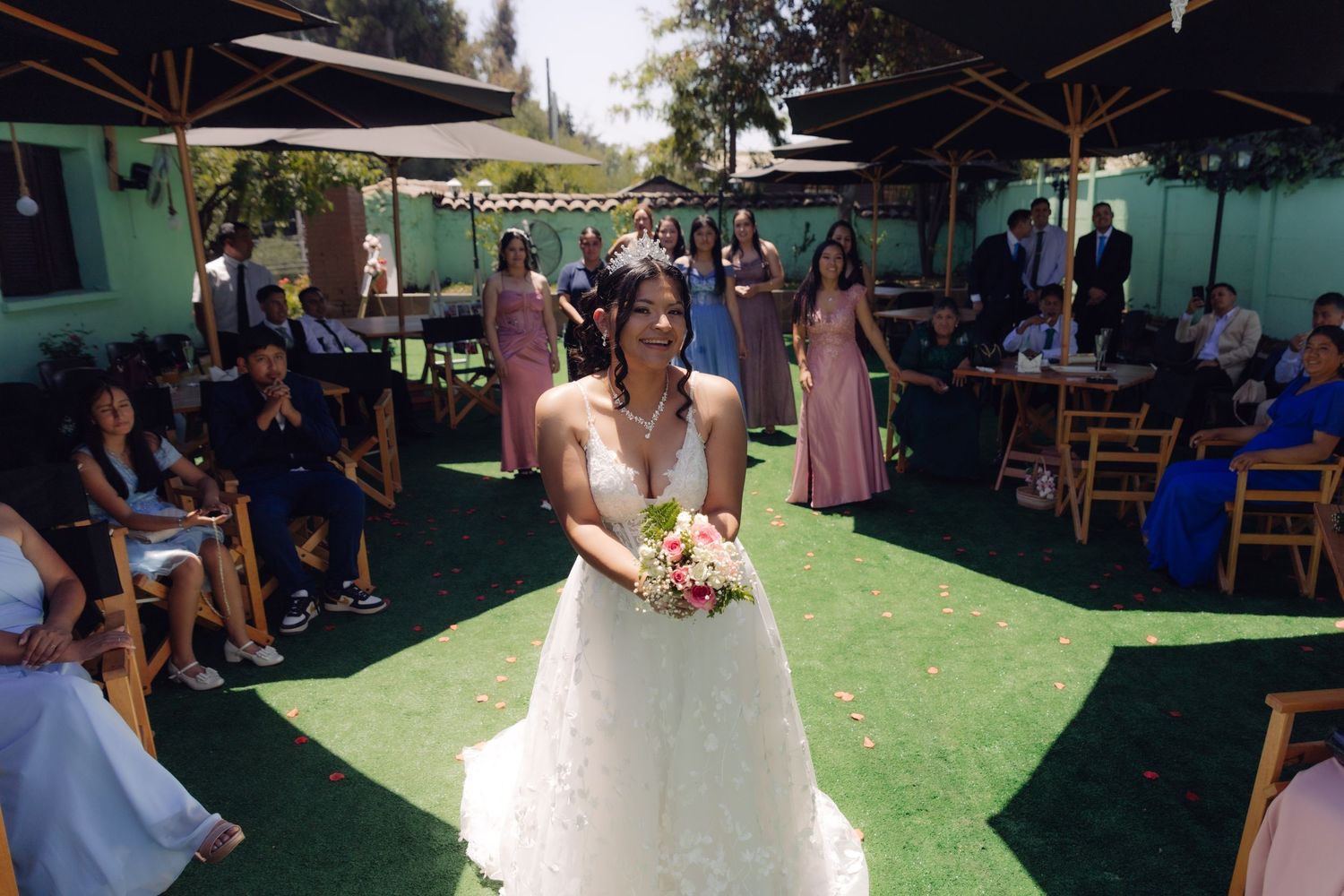 Bride in white gown prepares to toss bouquet to guests at outdoor wedding reception.