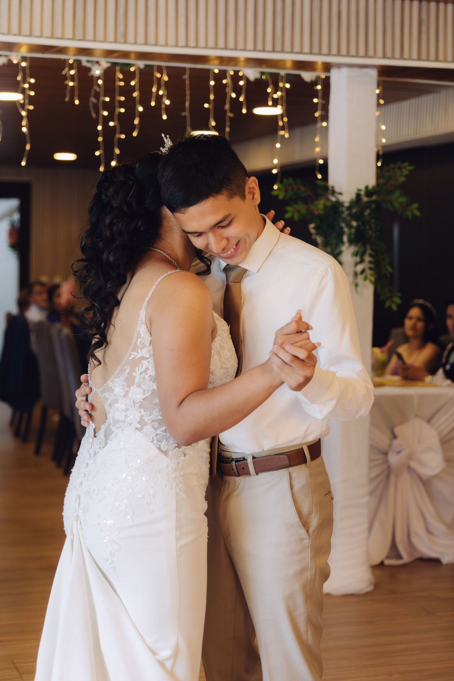 Smiling couple shares romantic first dance under warm string lights at wedding reception.