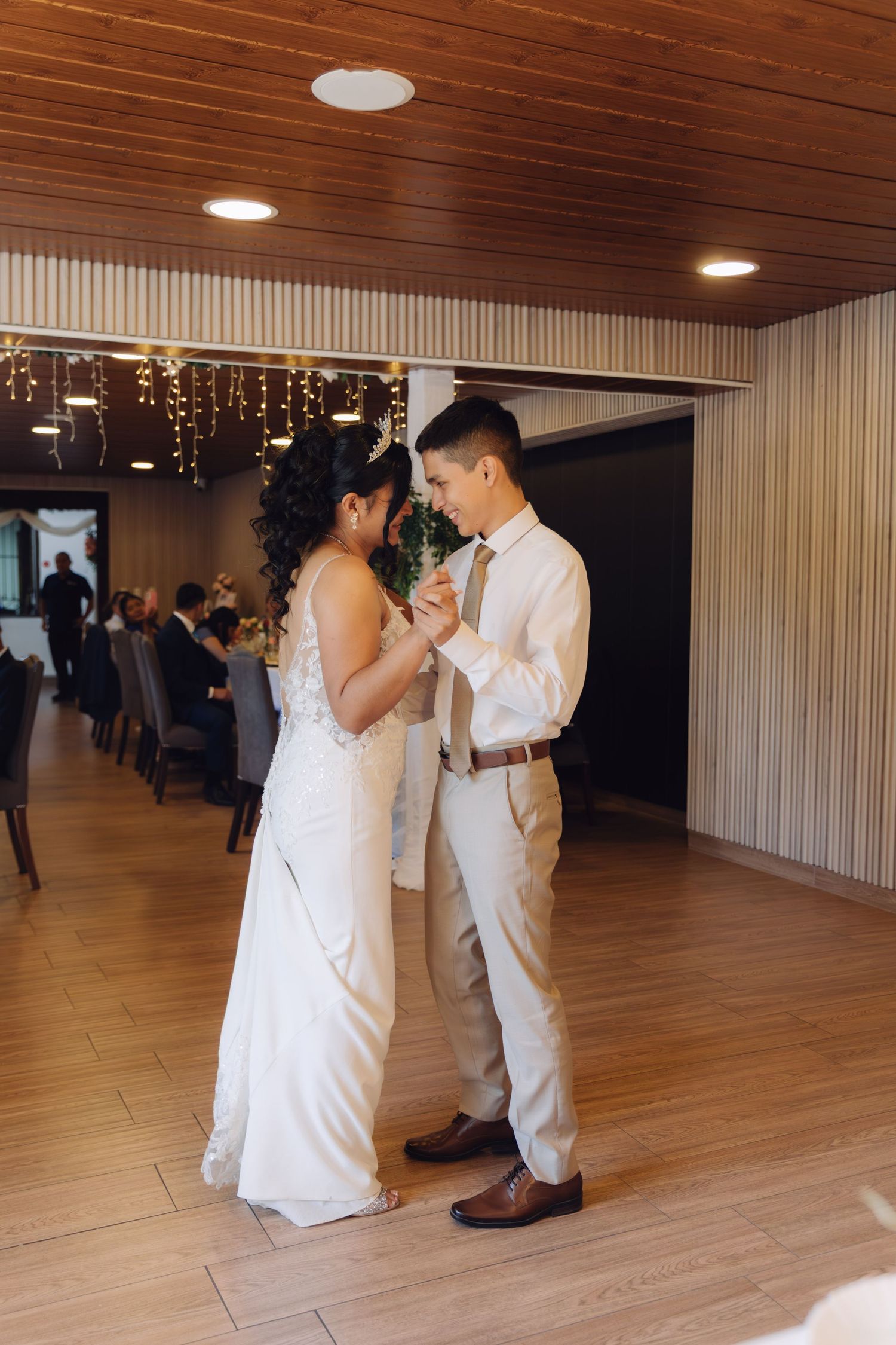 Bride and groom share first dance on wooden floor in elegantly decorated wedding venue.