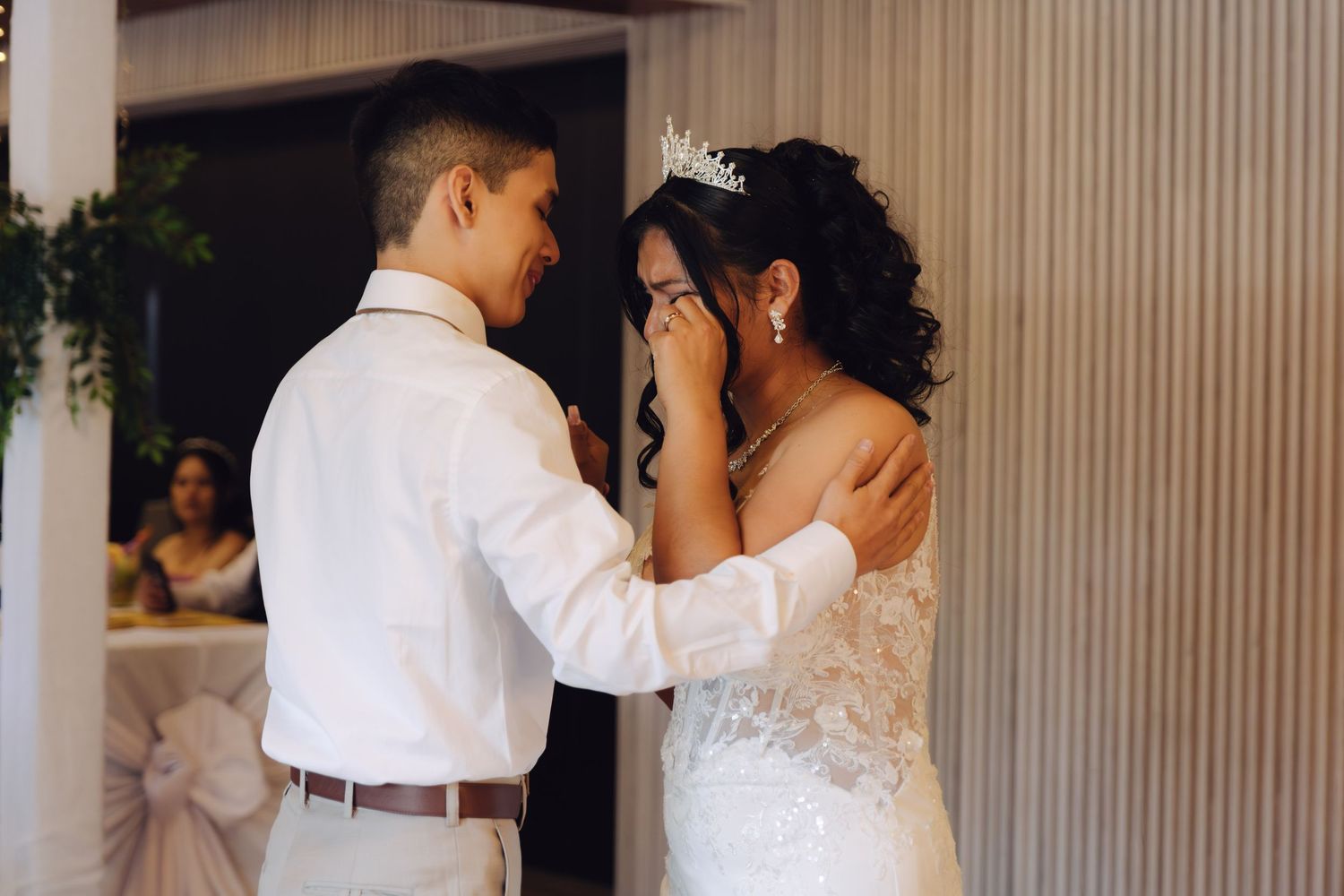 Emotional groom gently touches brides face during heartfelt first dance at wedding reception.
