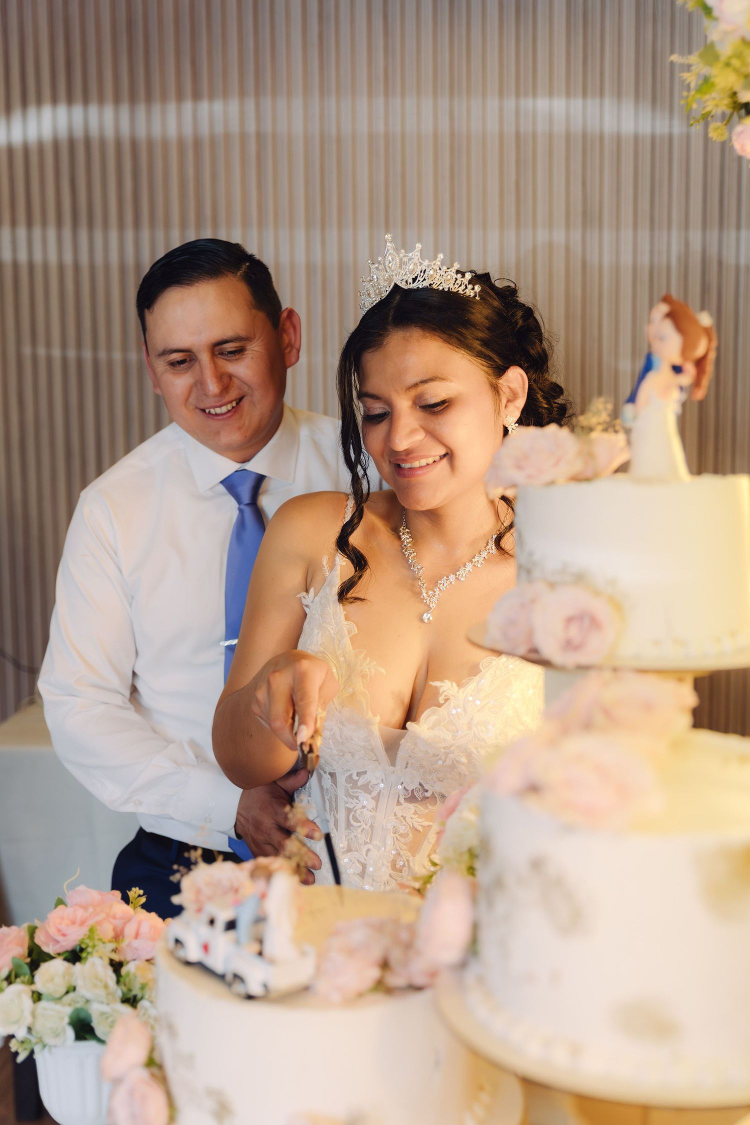 Smiling bride and groom cutting their elegant white tiered wedding cake decorated with pink roses.