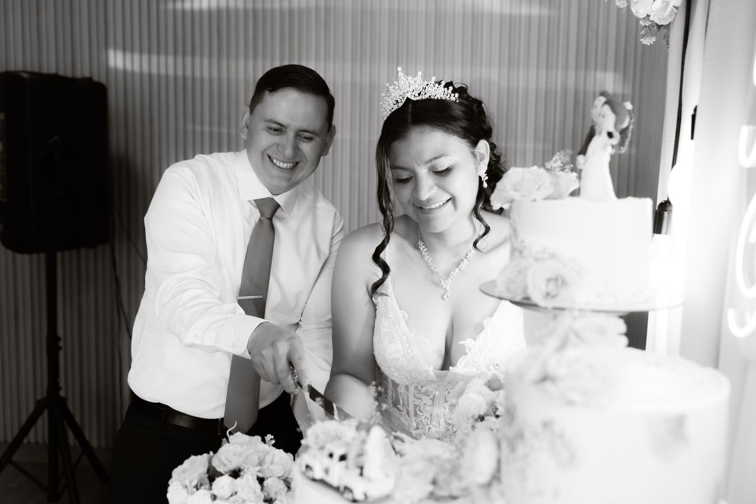 Black and white photo of laughing bride and groom cutting their decorated wedding cake together.