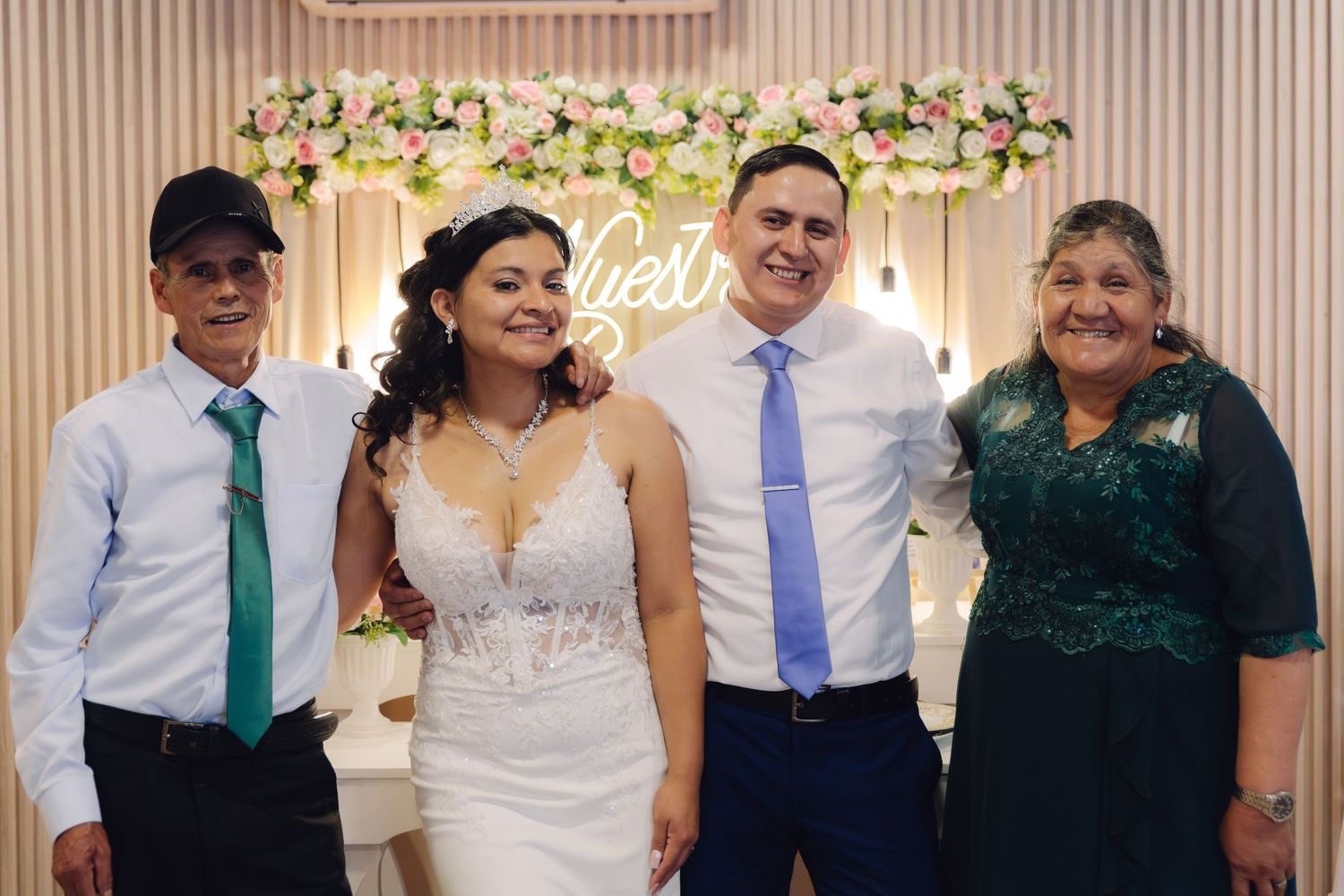 Wedding couple posing with two guests in front of floral backdrop at reception venue.