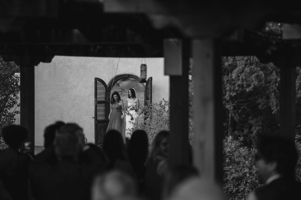 Black and white wedding photo of bride and groom standing in arched doorway, guests gathered in foreground.