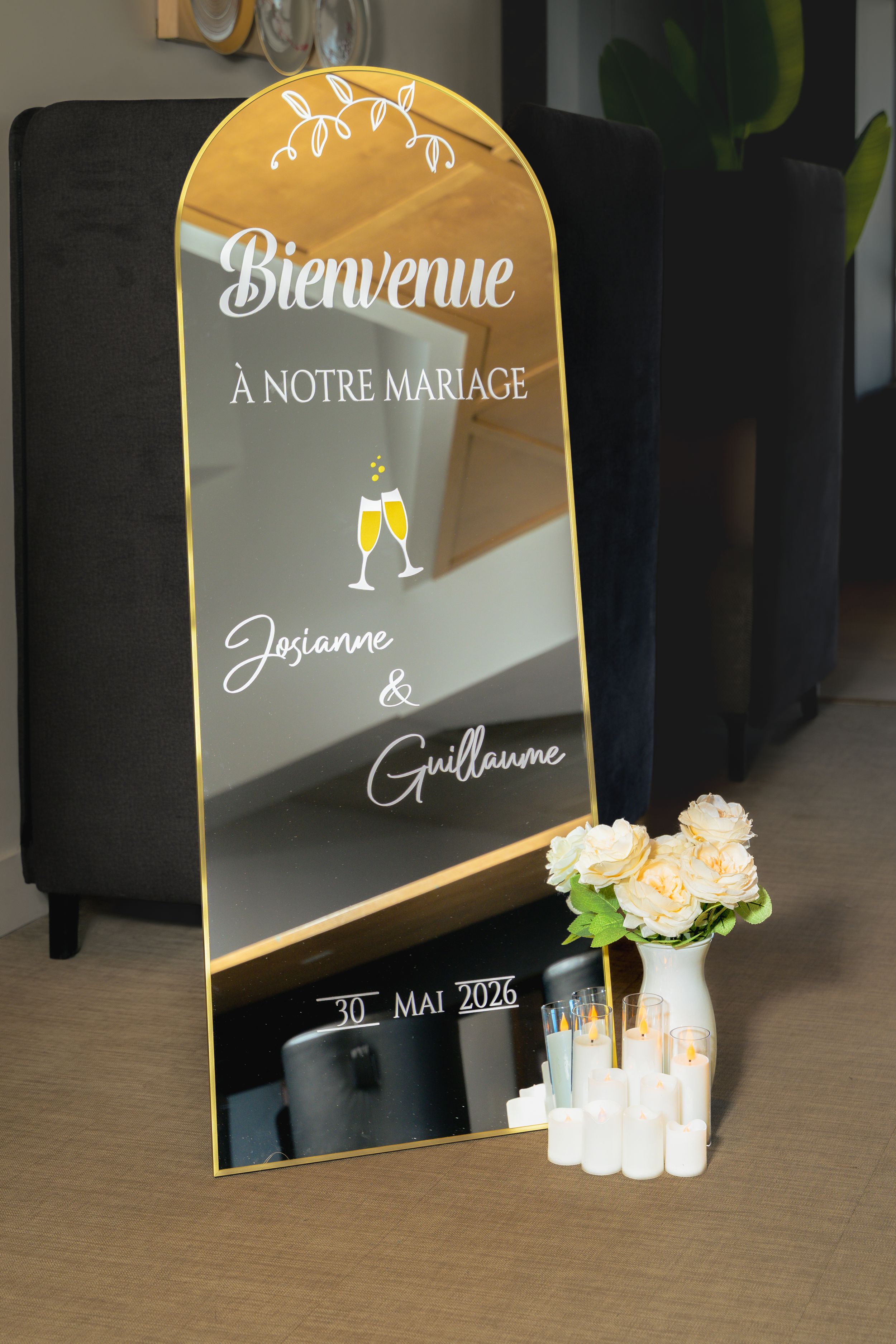 Miroir de bienvenue de mariage avec lettrage blanc, vase de fleurs roses et bougies allumées au sol.