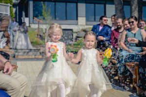 Deux petites filles d'honneur en robes blanches marchant dans l'allée du mariage avec des pistolets à bulles.