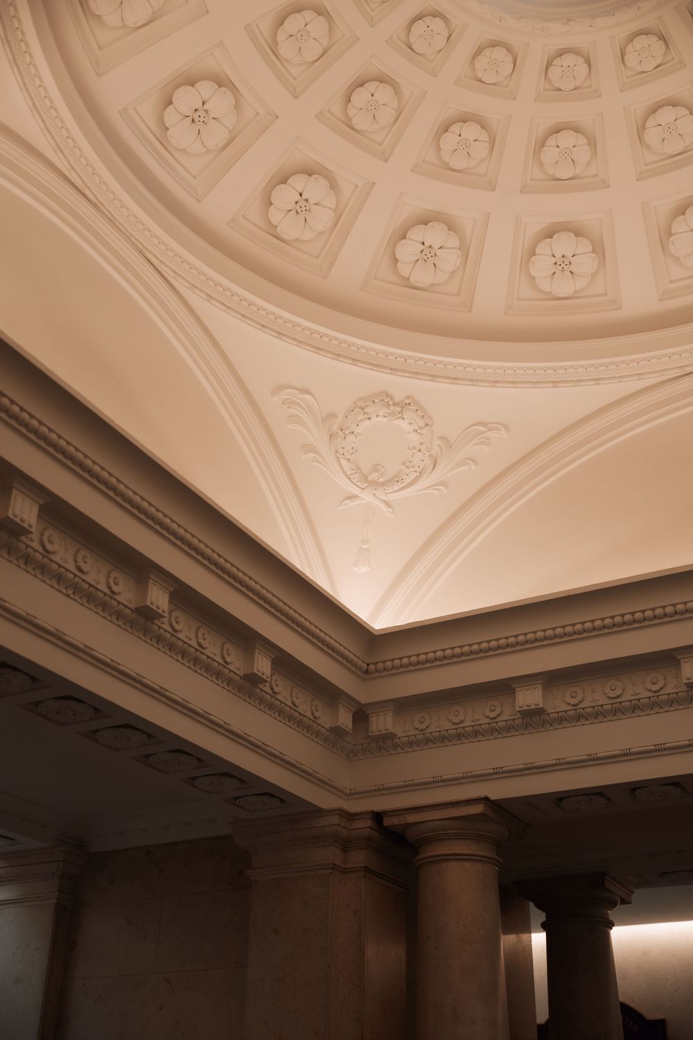 Ornate classical ceiling with coffered dome, floral plasterwork, decorative cornice, and stone columns in elegant architectural interior.