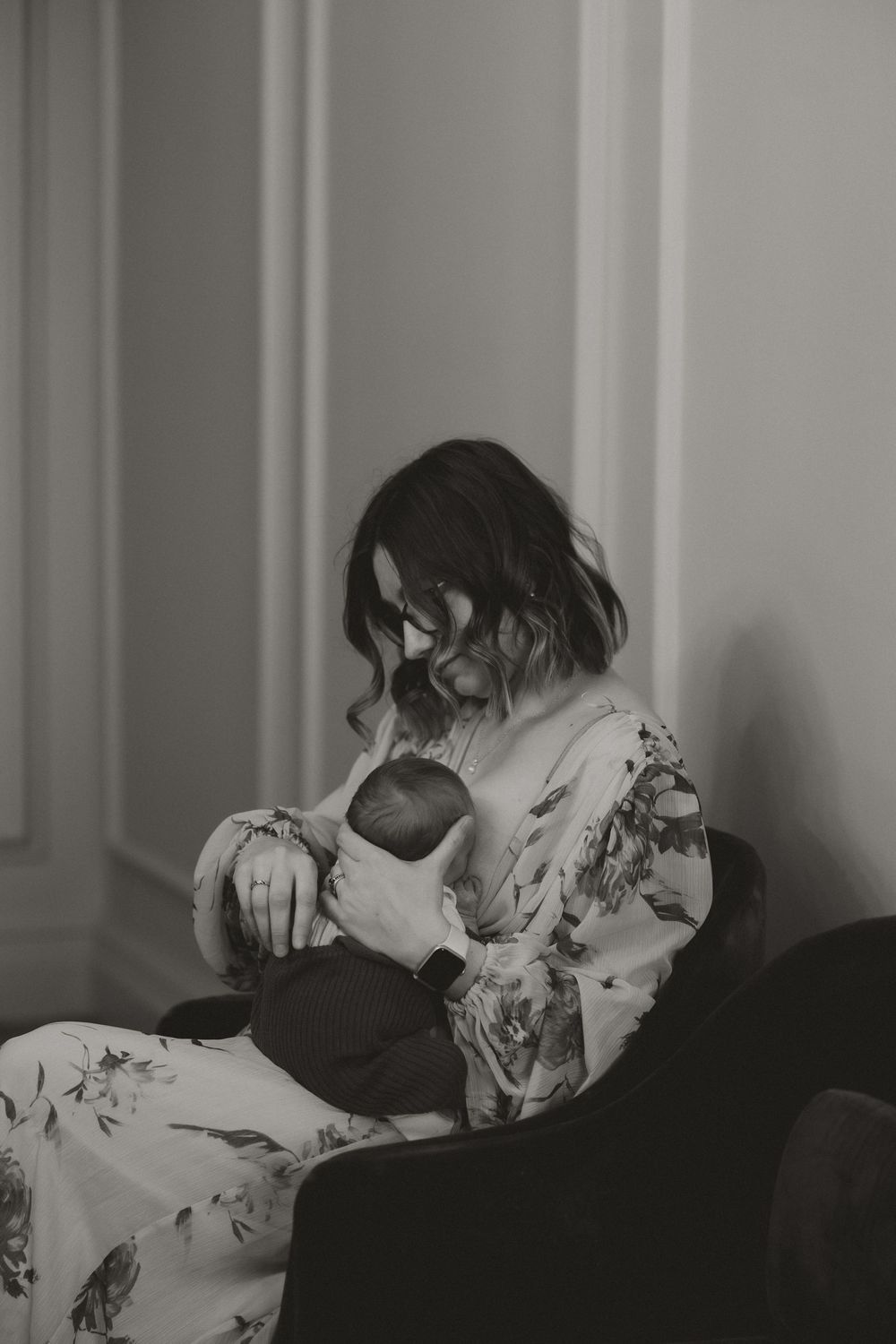 Black and white photo of a mother tenderly cradling her newborn baby while seated indoors.