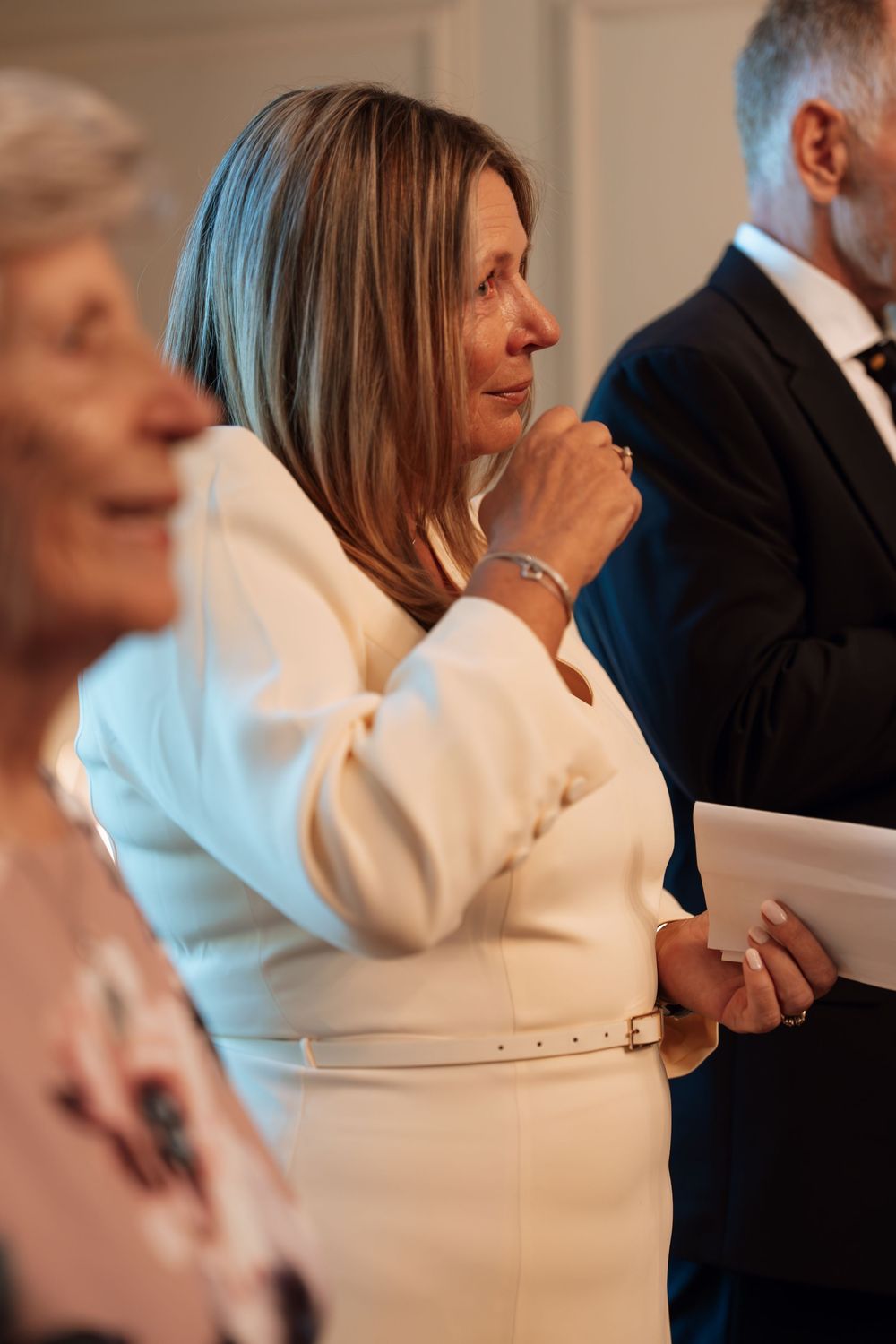 Emotional woman in white outfit at a wedding ceremony, holding hands and looking moved.