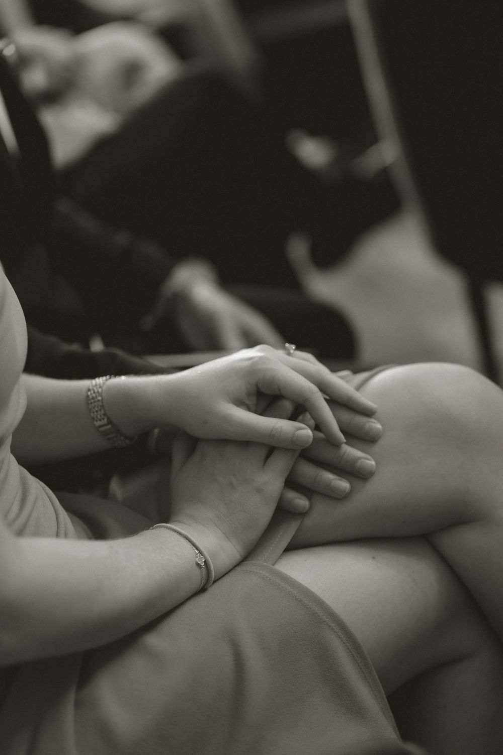 Black and white photo of two people holding hands tenderly, with bracelets visible, conveying comfort and connection.