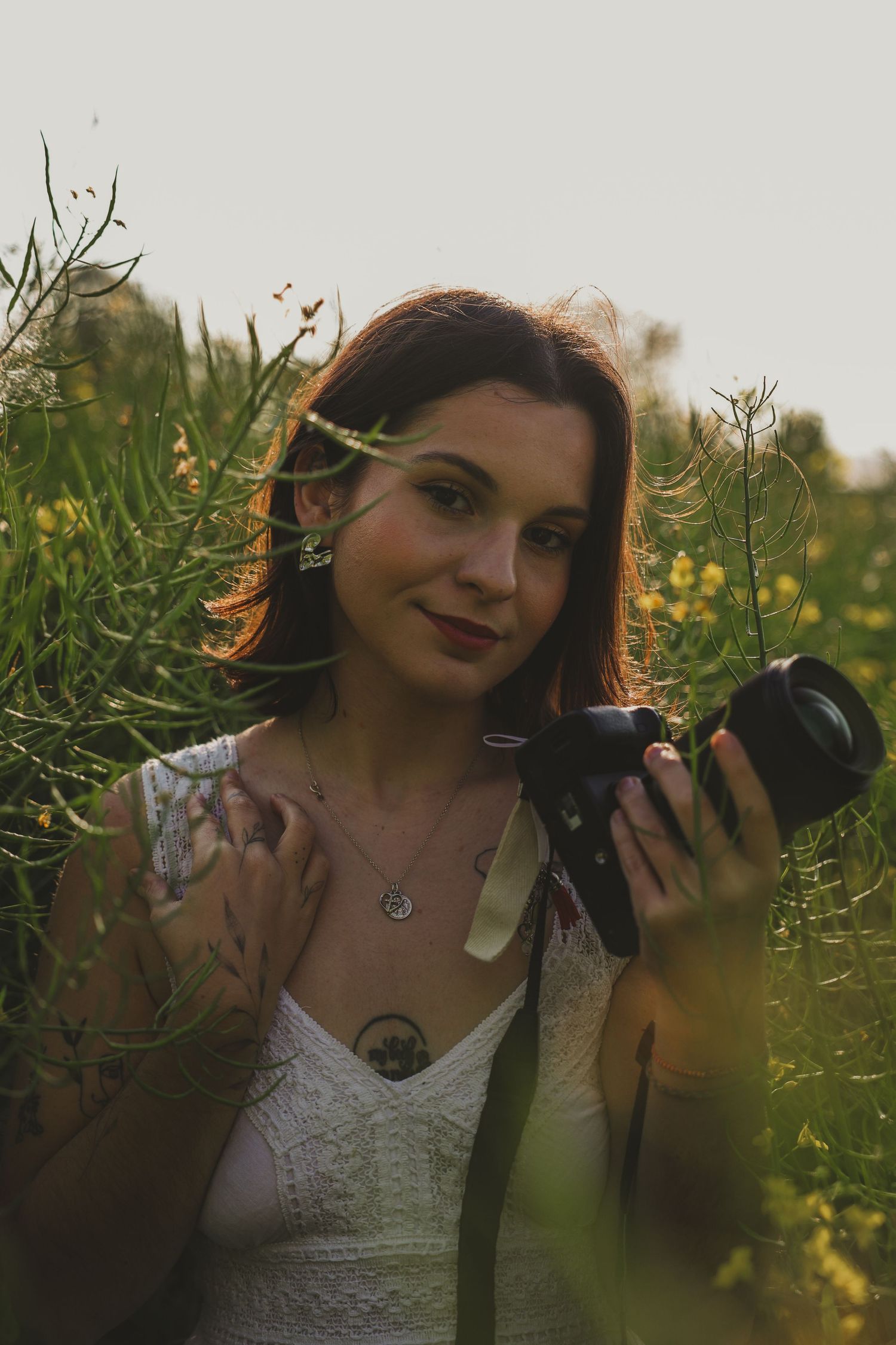 Jeune femme aux cheveux roux tenant une caméra dans un champ de plantes vertes à l'heure d'or.