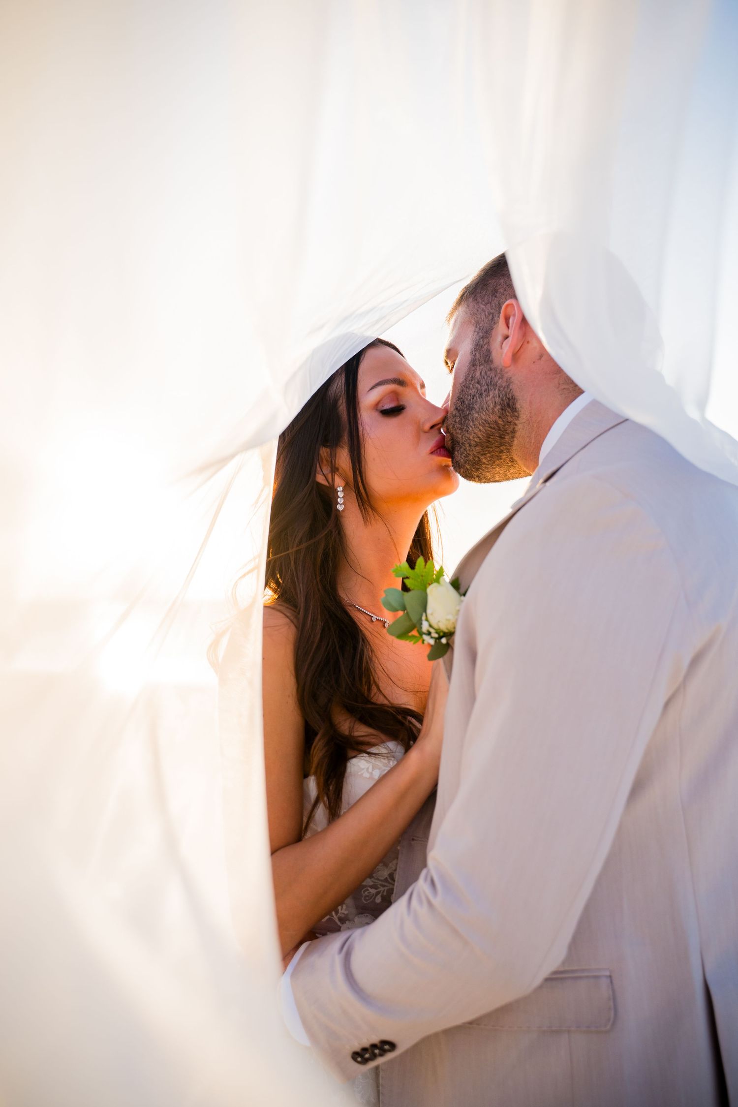 Bride and groom sharing a kiss beneath the wedding veil in warm golden light during a Mauritius beach wedding, Luminair Studio