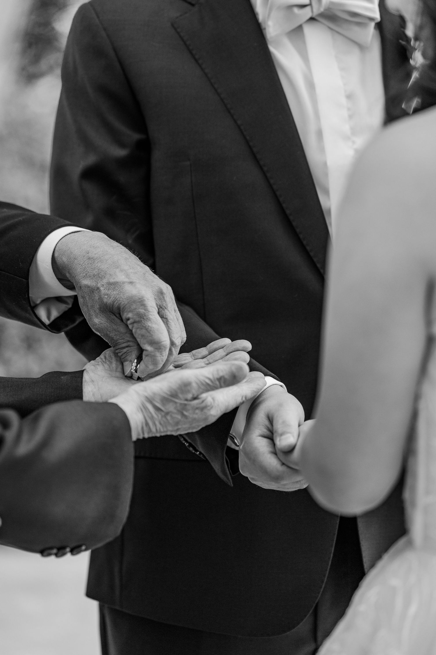 Black and white photo of groom placing wedding ring on bride's finger during ceremony.