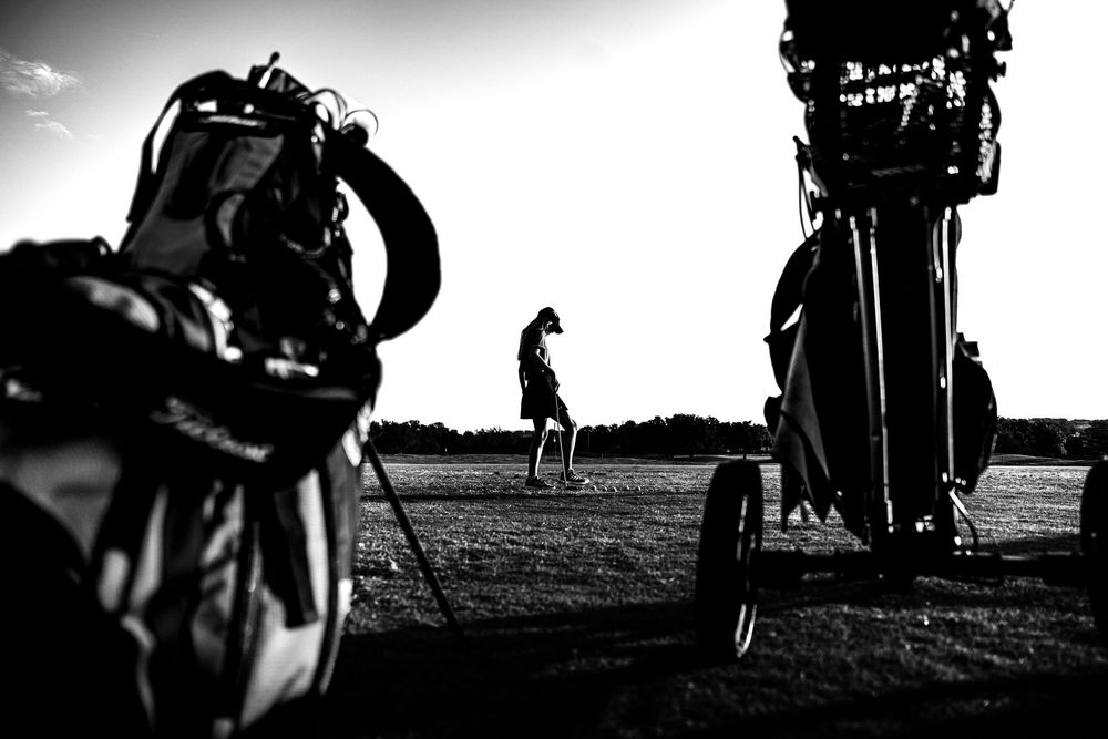 Black and white photo of golf bags framing a golfer on a course.