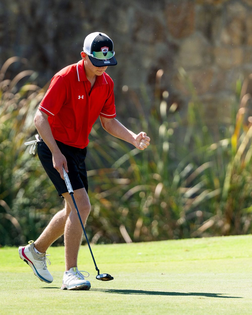 Young golfer in red Under Armour shirt celebrates putt on golf course green.