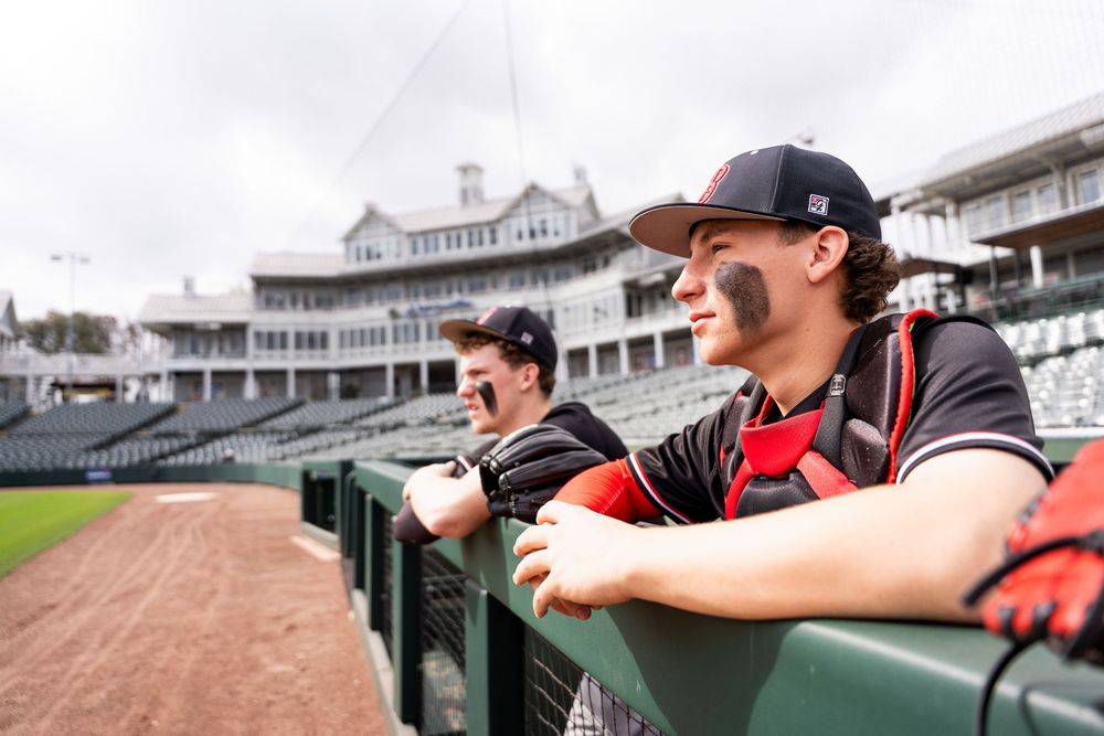 Two baseball players in black uniforms lean on dugout railing at a classic stadium.