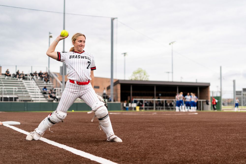 Softball pitcher in Braswell uniform winds up to throw on a green field.
