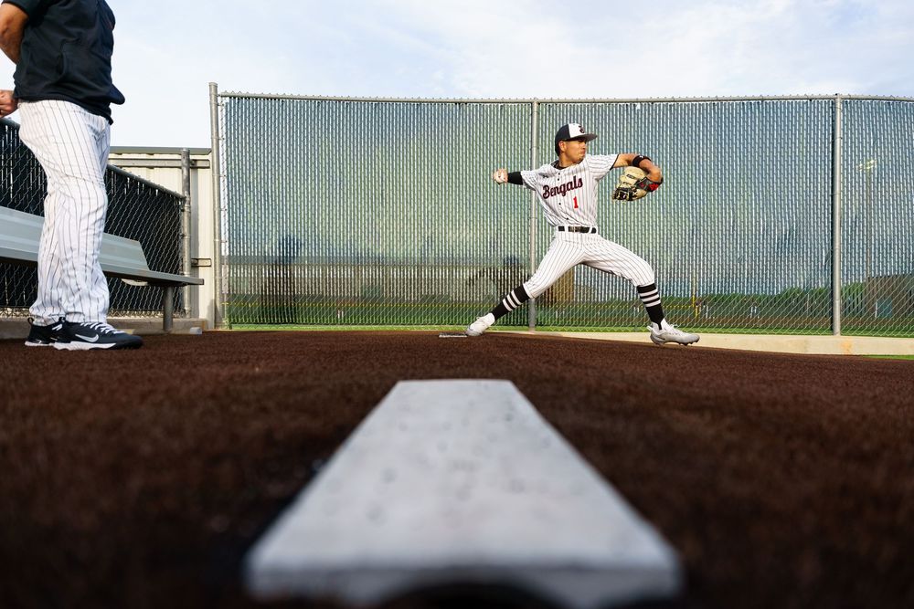 Baseball player throws ball on field photographed from low angle near dugout bench.