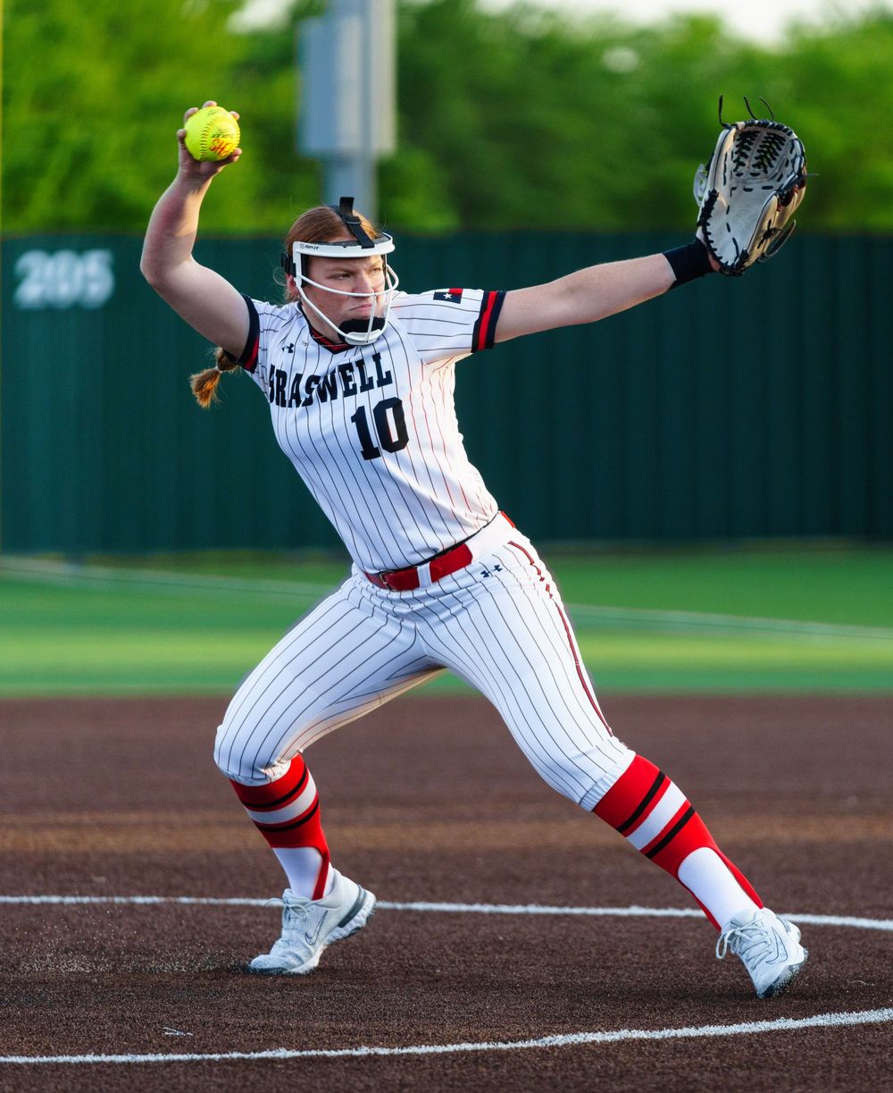 Braswell #10 softball pitcher winds up to throw a yellow ball during a game in white pinstripe uniform.