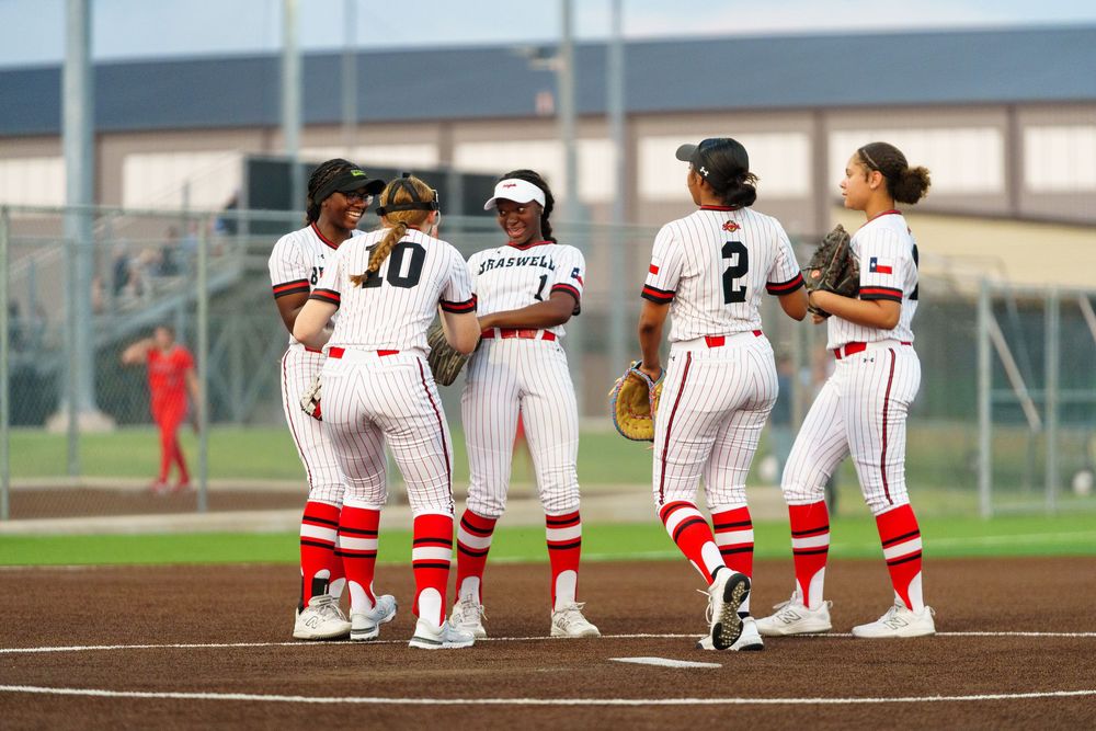 Braswell softball team players huddle together on the field in white pinstripe uniforms during a game.