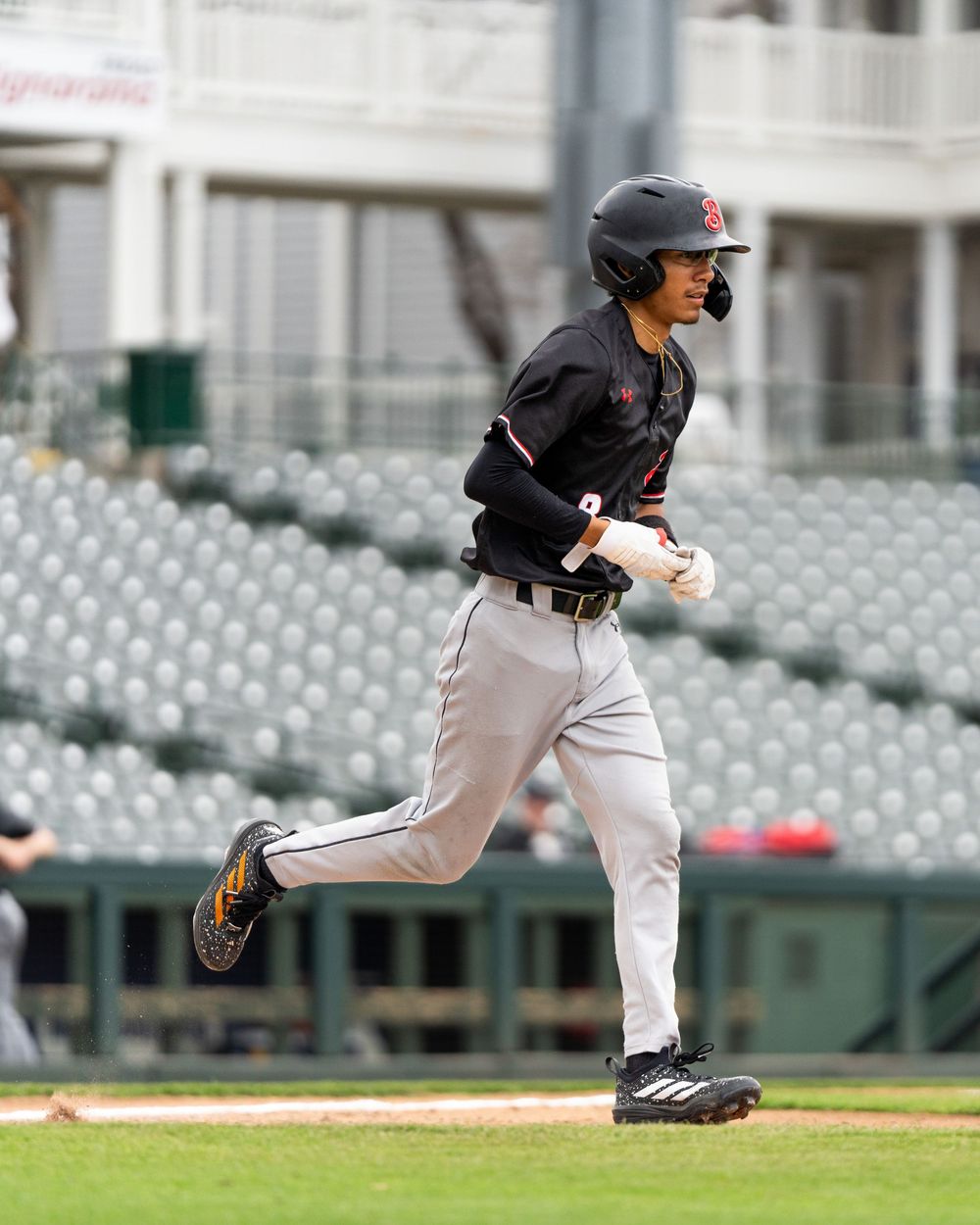 Baseball player in gray away uniform runs the bases at a professional stadium with empty seats.