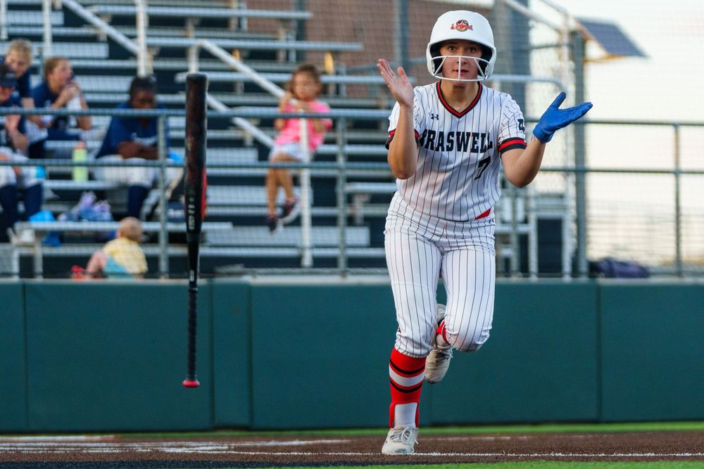 Braswell softball player sprints the bases in white pinstripe uniform with red socks during a game.