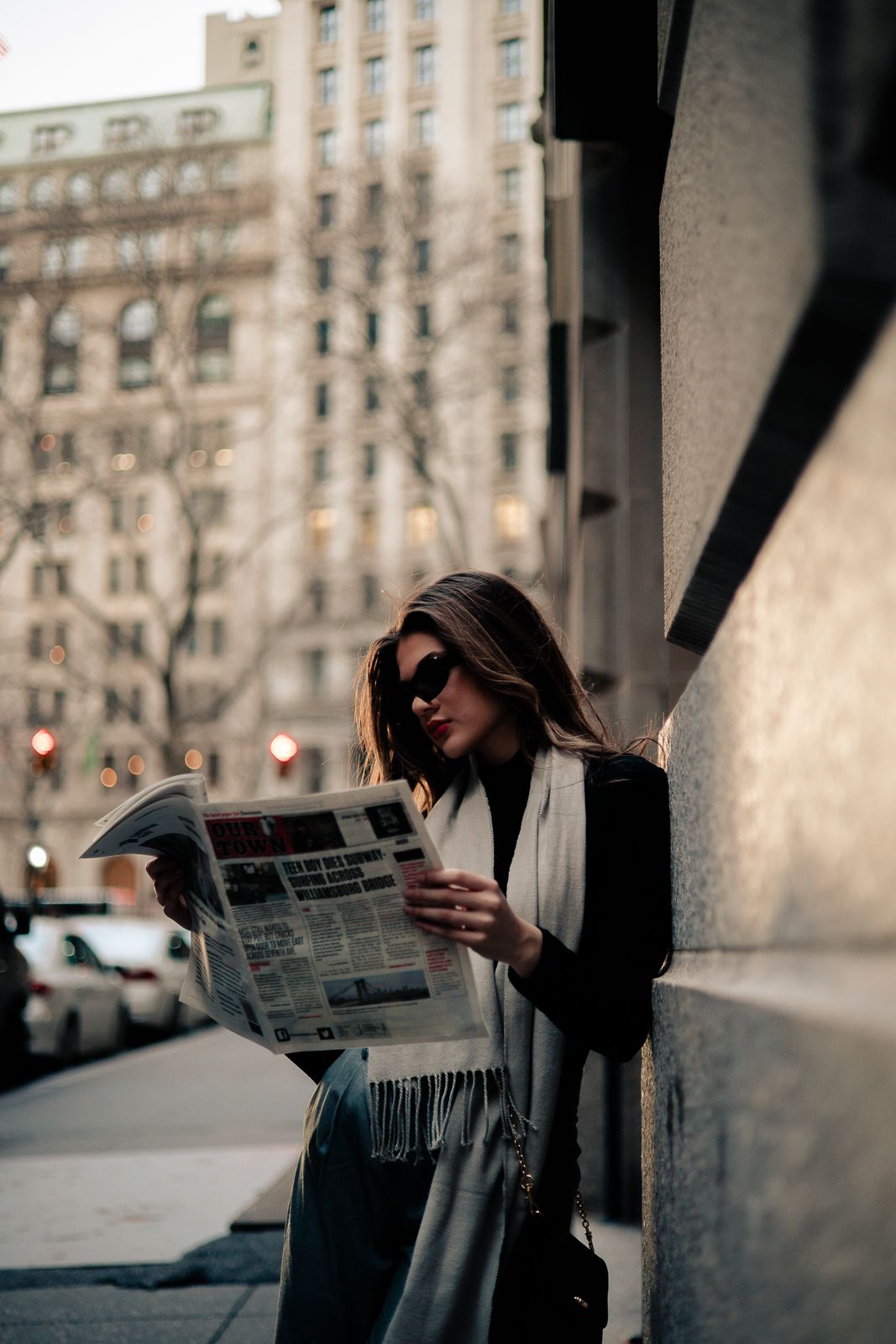 Woman reading a newspaper on a city sidewalk beside stone buildings, New York City | Mannyportraits
