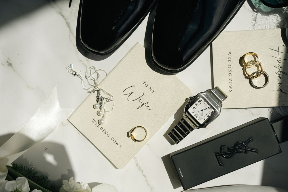 Elegant wedding flat lay with dress shoes, Cartier watch, gold rings, YSL wallet, and a To My Wife card on marble.