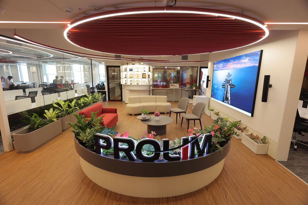 Modern PROLIM office lobby with red neon lighting, green plants, lounge seating, and a large video display wall.