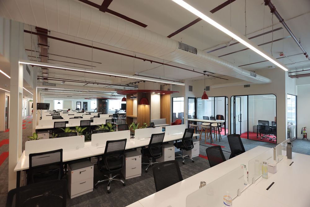 Modern open-plan office with white desks, black chairs, bright lighting, and glass partitions in a contemporary workspace.