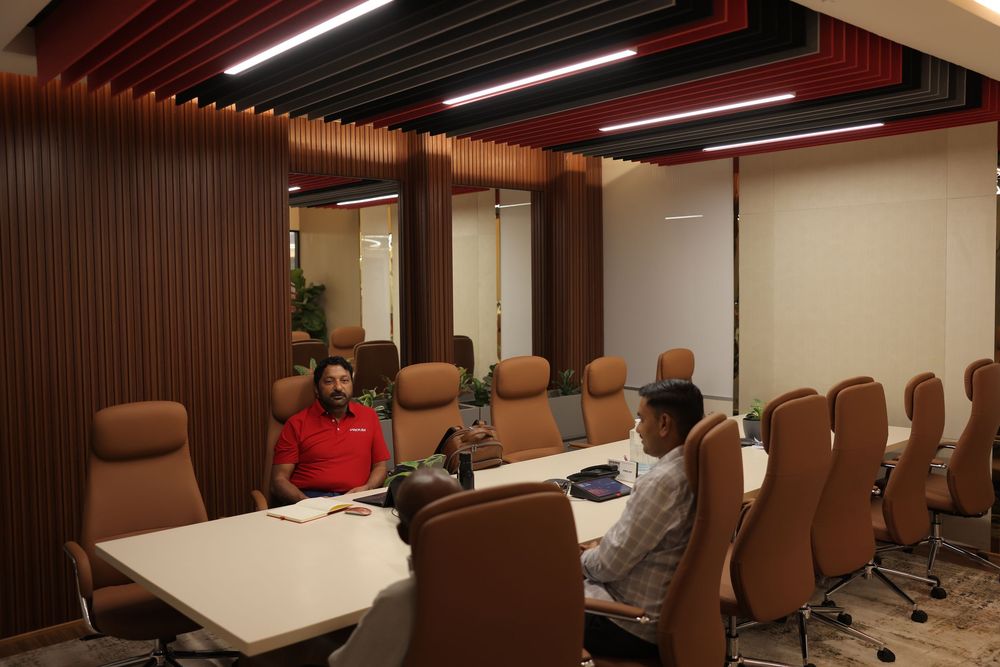 Two professionals meeting in a modern conference room with brown leather chairs and wooden wall panels.