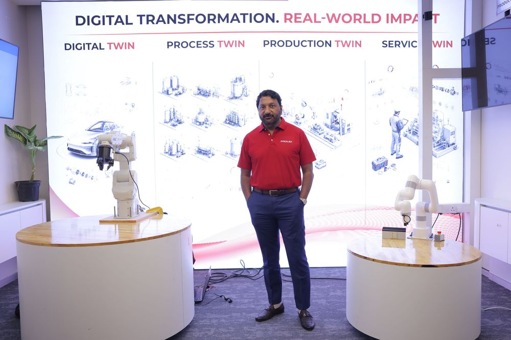Man stands before a Digital Transformation display with robotic arms, showcasing Digital Twin and Production Twin technology solutions.