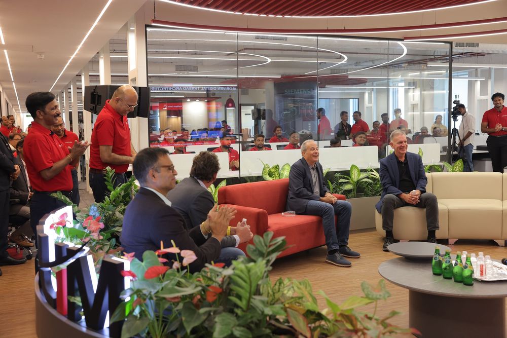 Corporate event in a modern office with red decor, attendees in red shirts gathered around sofas and workstations.