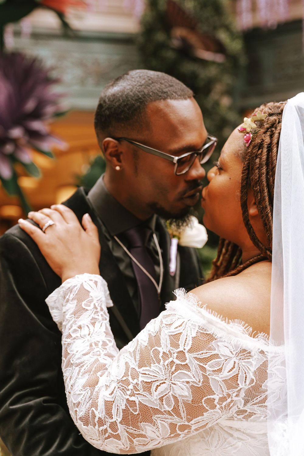 A Black bride and groom share an intimate moment at their wedding ceremony, dressed in lace gown and dark suit.