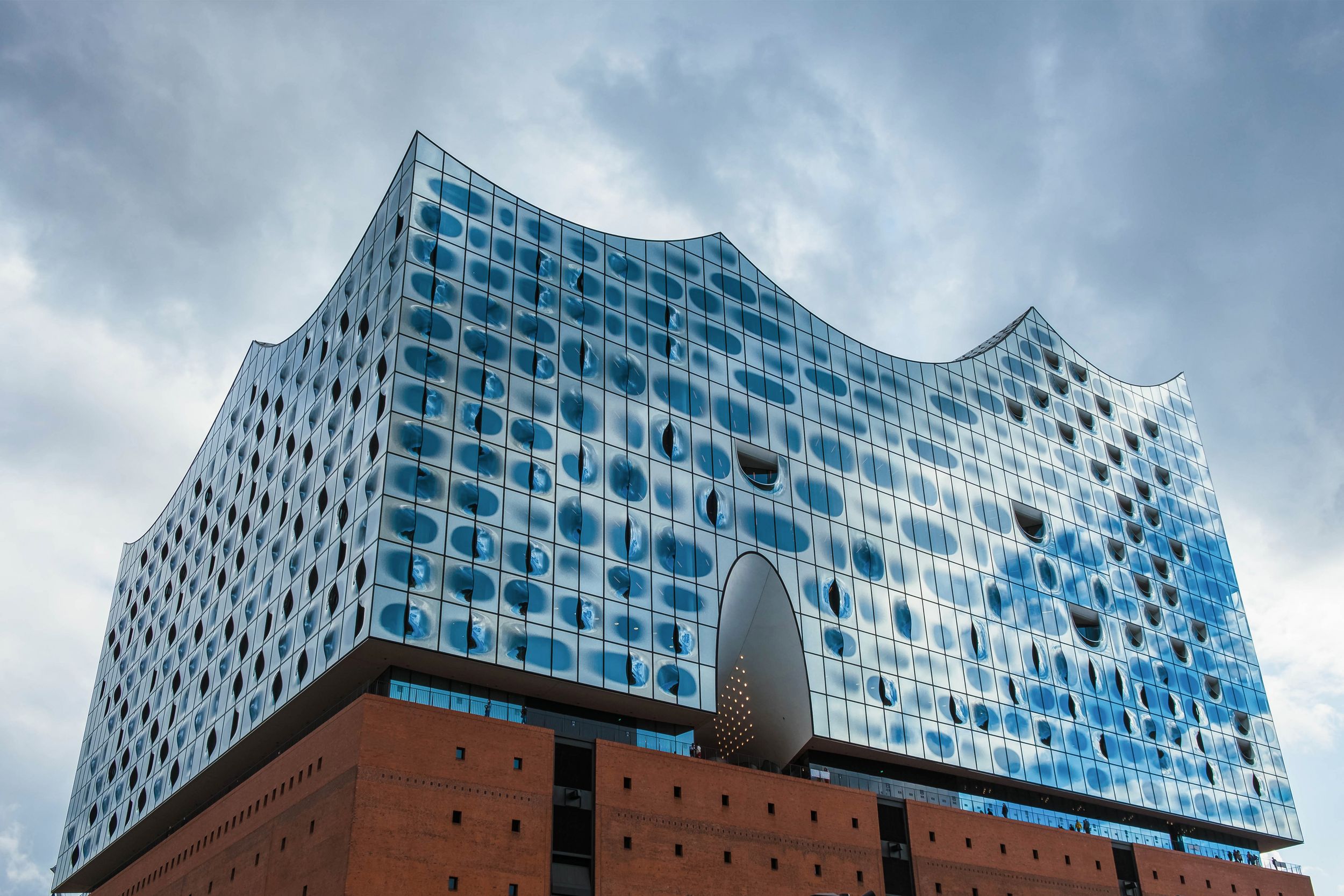 Moderní skleněná fasáda Elbphilharmonie v Hamburku fotografovaná z podhledu.