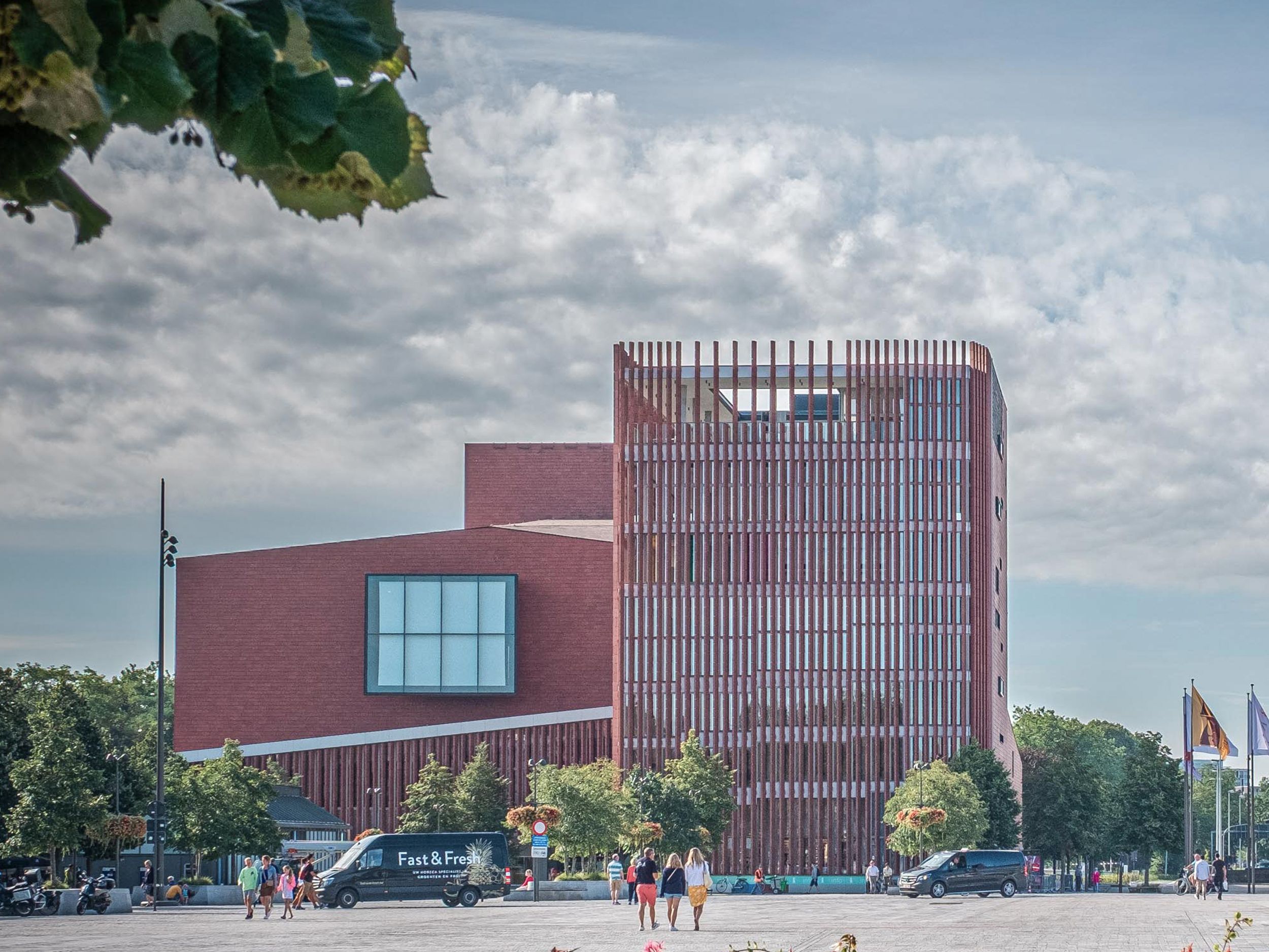 Moderní červená budova s vertikálními lamelami na městském náměstí.